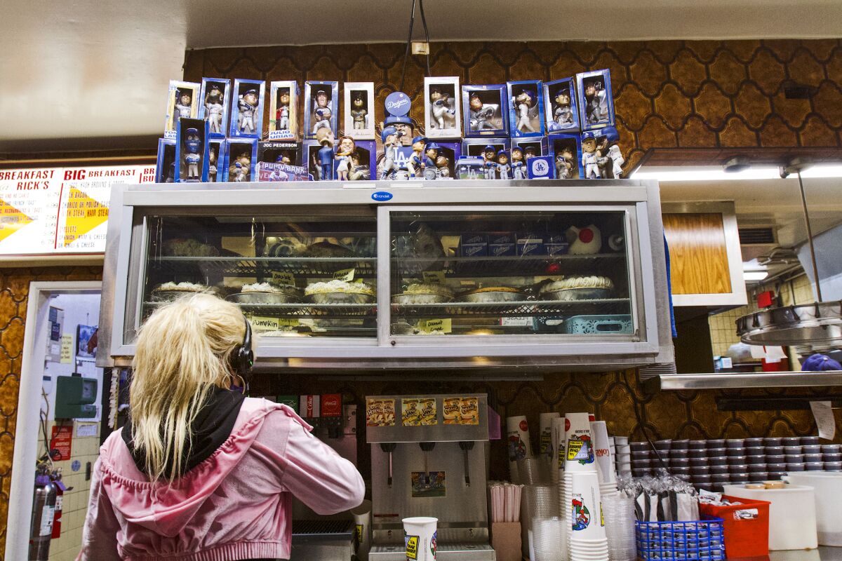 A photo of a server inside Rick's readying an order underneath the pie case, which is lined with rows of Dodgers bobbleheads.