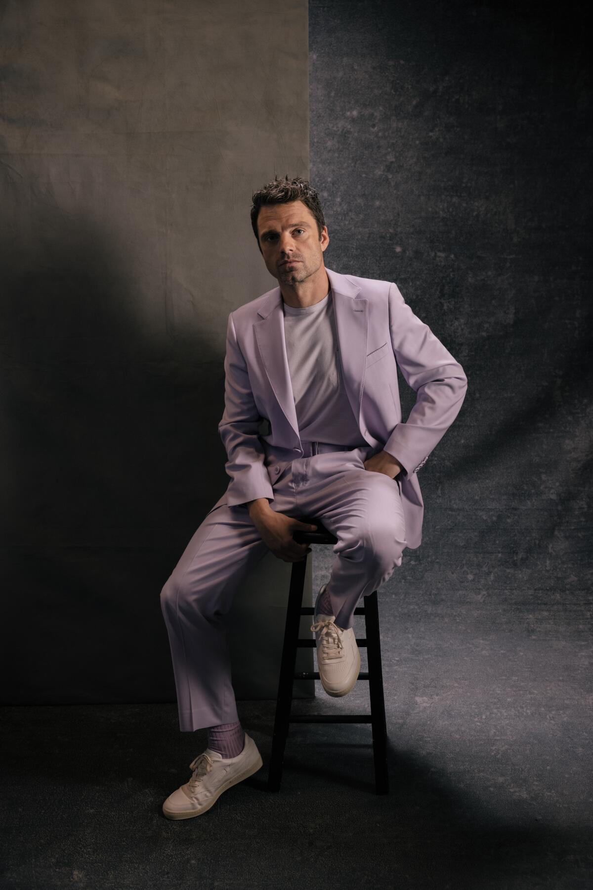 Sebastian Stan perches on a stool for a portrait.