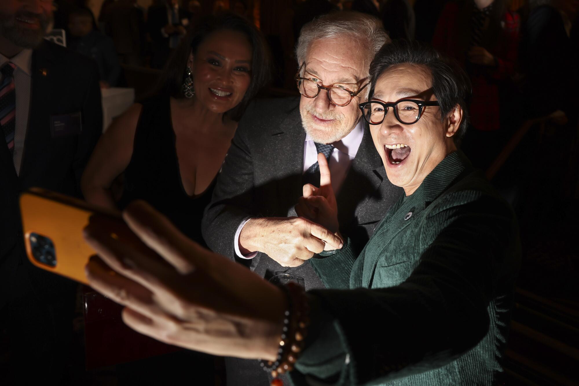 A woman in the shadows next to a smiling older man and a beaming young man.