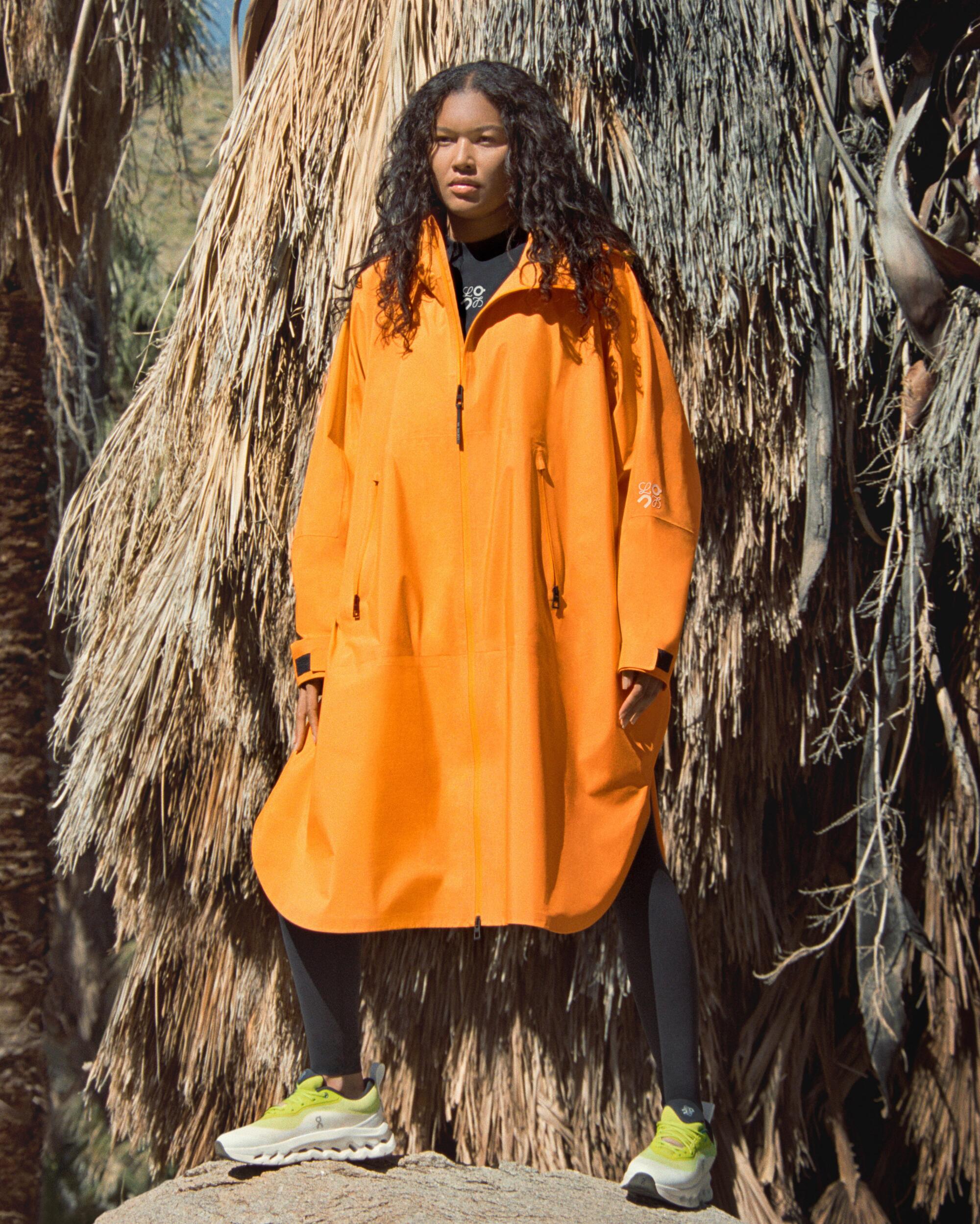 A person stands outdoors wearing a large orange coat.