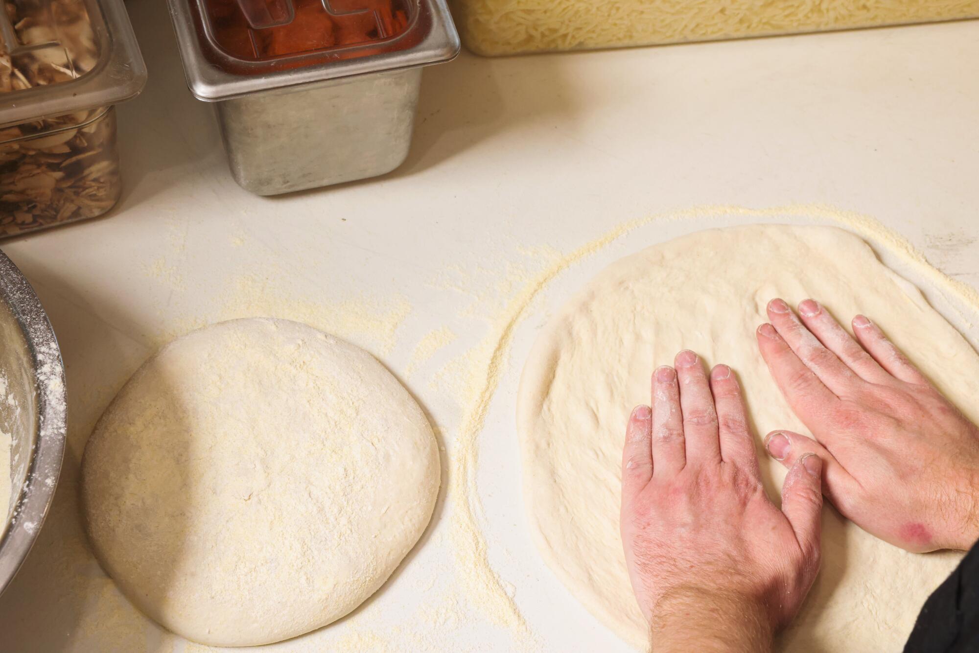 A man's hands shape dough into flat circles for pizza.