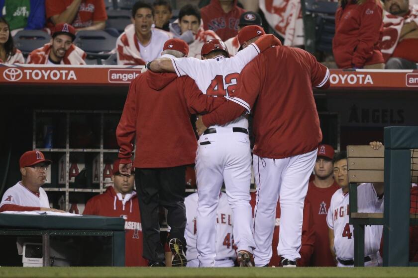 Kole Calhoun, center, is helped off the field by Manager Mike Scioscia, right, and assistant athletic trainer Rick Smith during the 11th inning of the Angels' 10-9 loss to the Athletics.