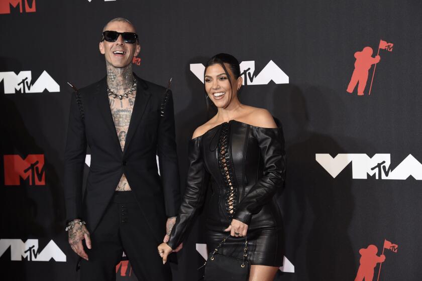 Travis Barker, left, and Kourtney Kardashian  hold hands while laughing while posing on a red carpet
