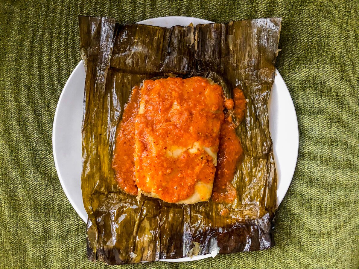 A tamale topped with red salsa on a banana leaf.