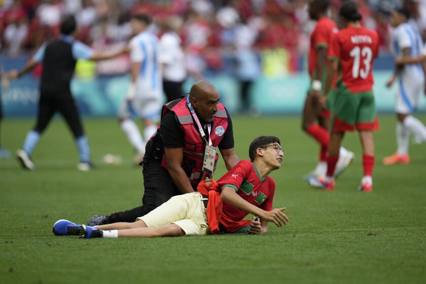 A steward catches a pitch invader during the men's Group B soccer match between Argentina and Morocco at Geoffroy-Guichard Stadium at the 2024 Summer Olympics, Wednesday, July 24, 2024, in Saint-Etienne, France. (AP Photo/Silvia Izquierdo)