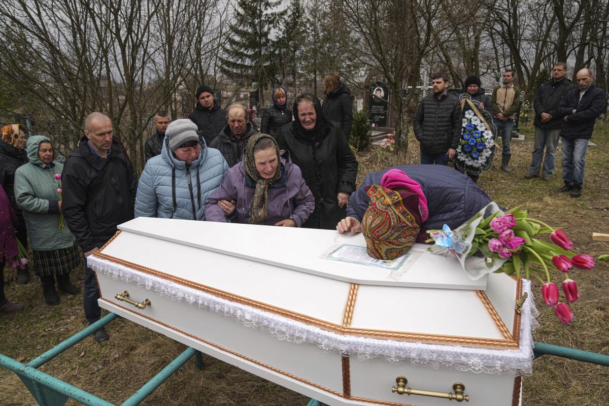 A woman puts her head down on a white casket while other people dressed in winter coats stand near her 