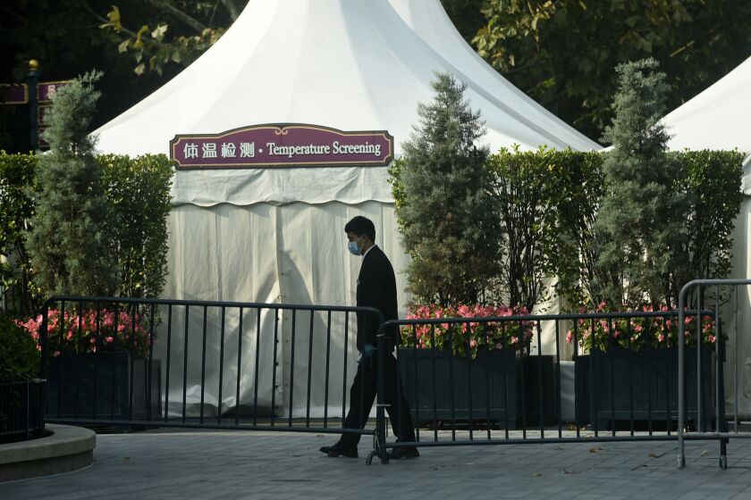 A worker wearing a face mask to help protect from the coronavirus walks by a closed temperature screening booth set up at the entrance gate to the Shanghai Disney Resort in Shanghai, China, Monday, Nov. 1, 2021. The theme park locked down late Sunday after learning a recent visitor had tested positive in another province. The park is shut for Monday and Tuesday as they continue to cooperate with the pandemic prevention efforts, Shanghai Disneyland said in a notice on Monday. (Chinatopix via AP)