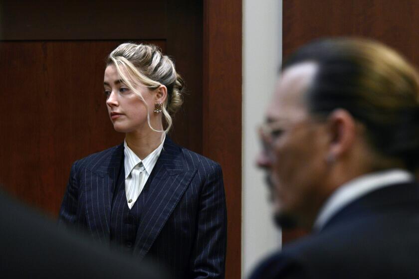 In a courtroom, a woman is in focus in the background while a man appears blurred in profile in the foreground