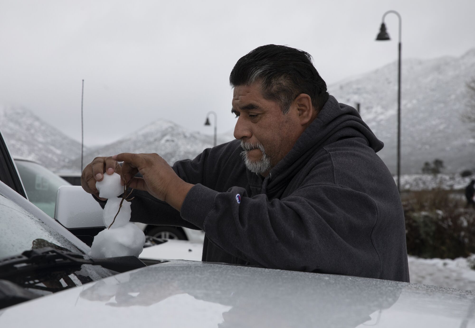 Emilio González, de 50 años, de San Diego, hace un muñeco de nieve encima de un vehículo 