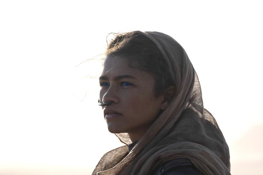 A woman in a desert wearing a tan headscarf, bodysuit and nose tube