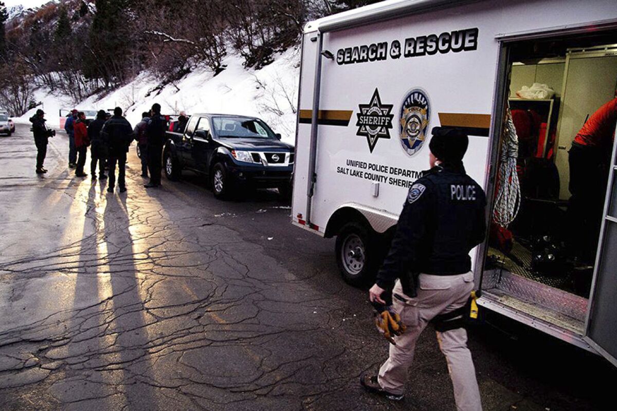 Emergency crews gather on a road next to a snow-covered hill and vehicles.