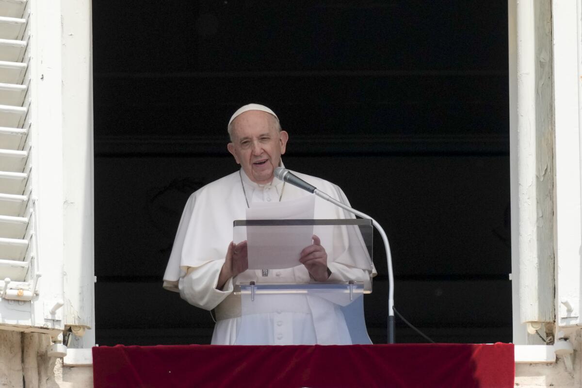 Pope Francis stands at a window with a clear glass lectern and microphone.