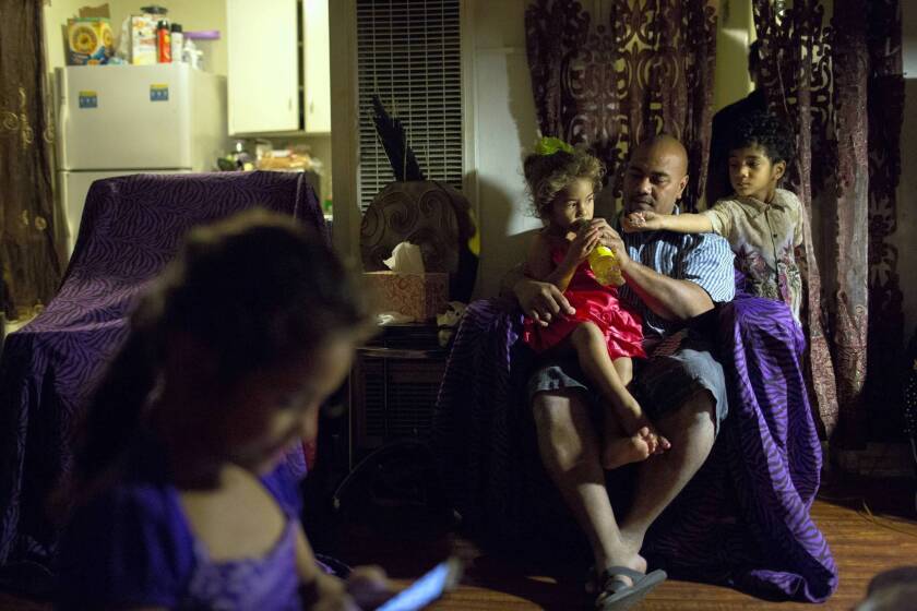 After church, Saia Holani sits with two of his children, 3-year-old Ana and 4-year-old Kaho, right, in the family's apartment in Inglewood. Katisha, 6, sits nearby.