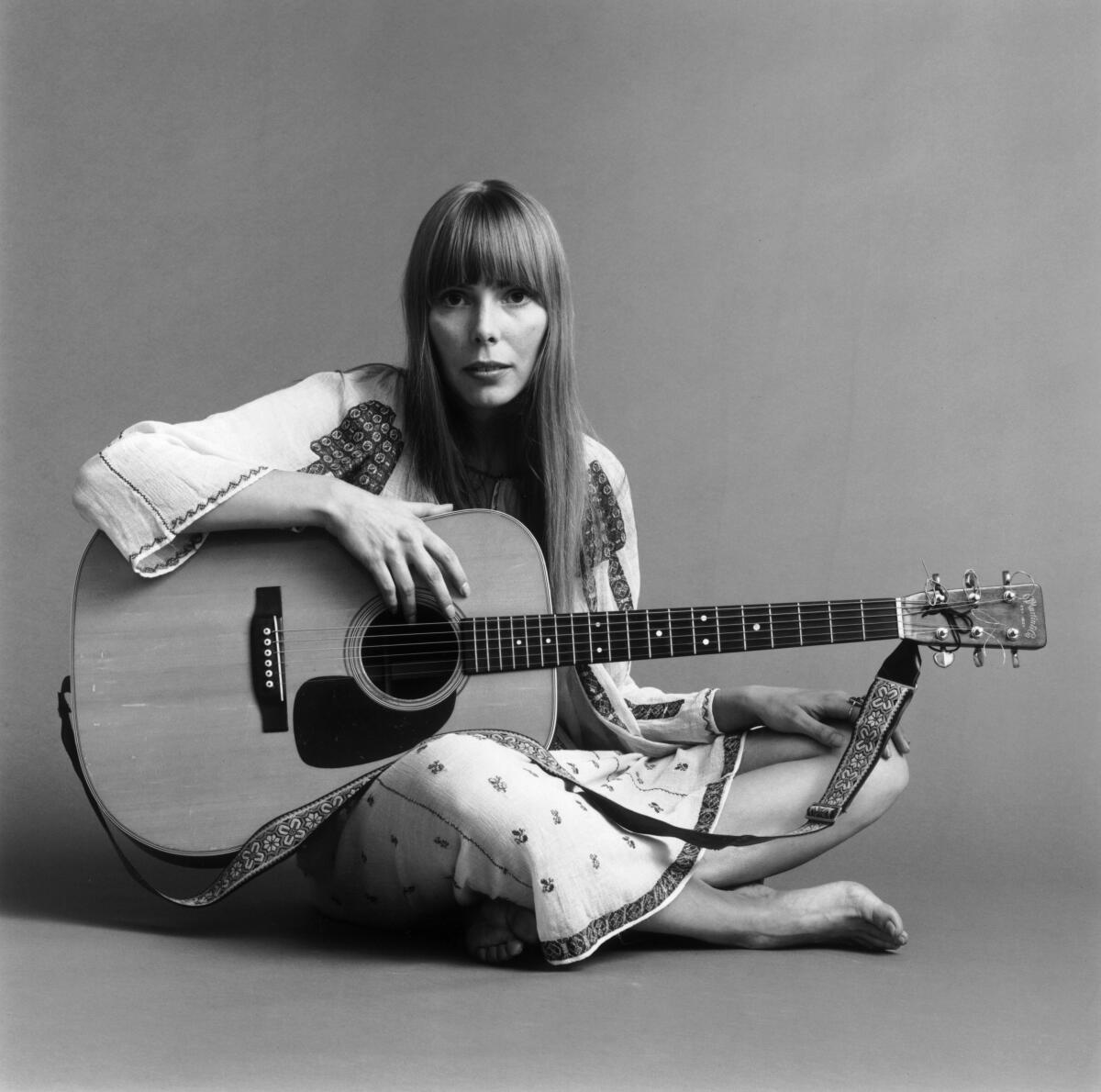 Portrait of Joni Mitchell seated on the floor with her acoustic guitar in her lap