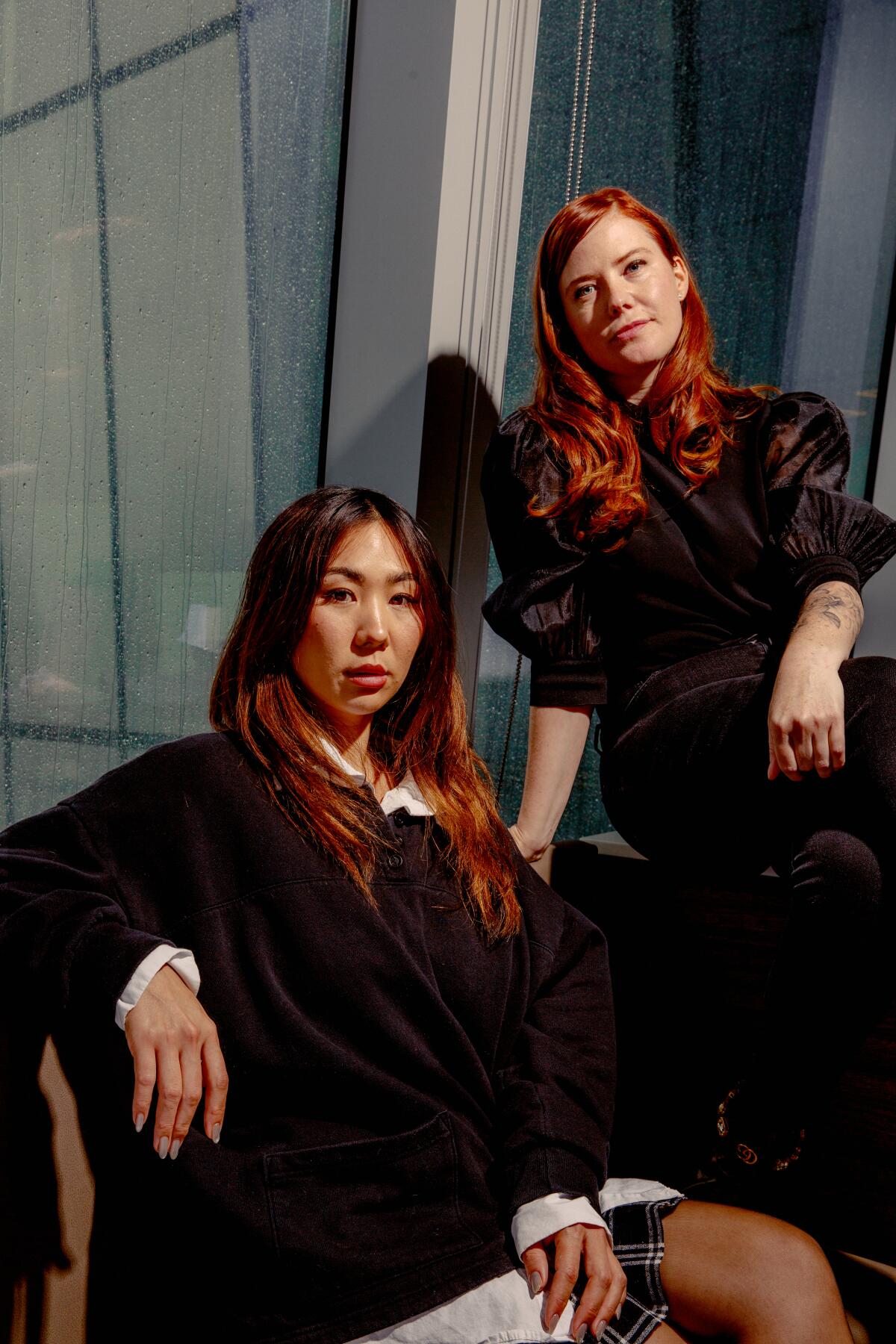 Rachel Lee sits on a chair next to Erin Lee Carr, who is seated above her to the right against a window.