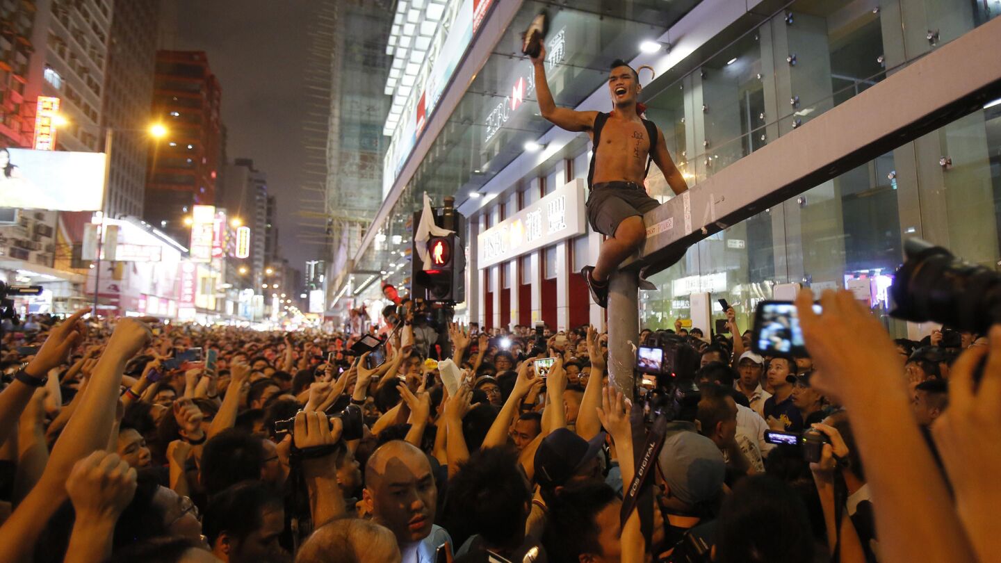 A pro-democracy student protester scales a traffic light pole in defiance of local residents demanding them to leave their occupied roads in Hong Kong on Friday.