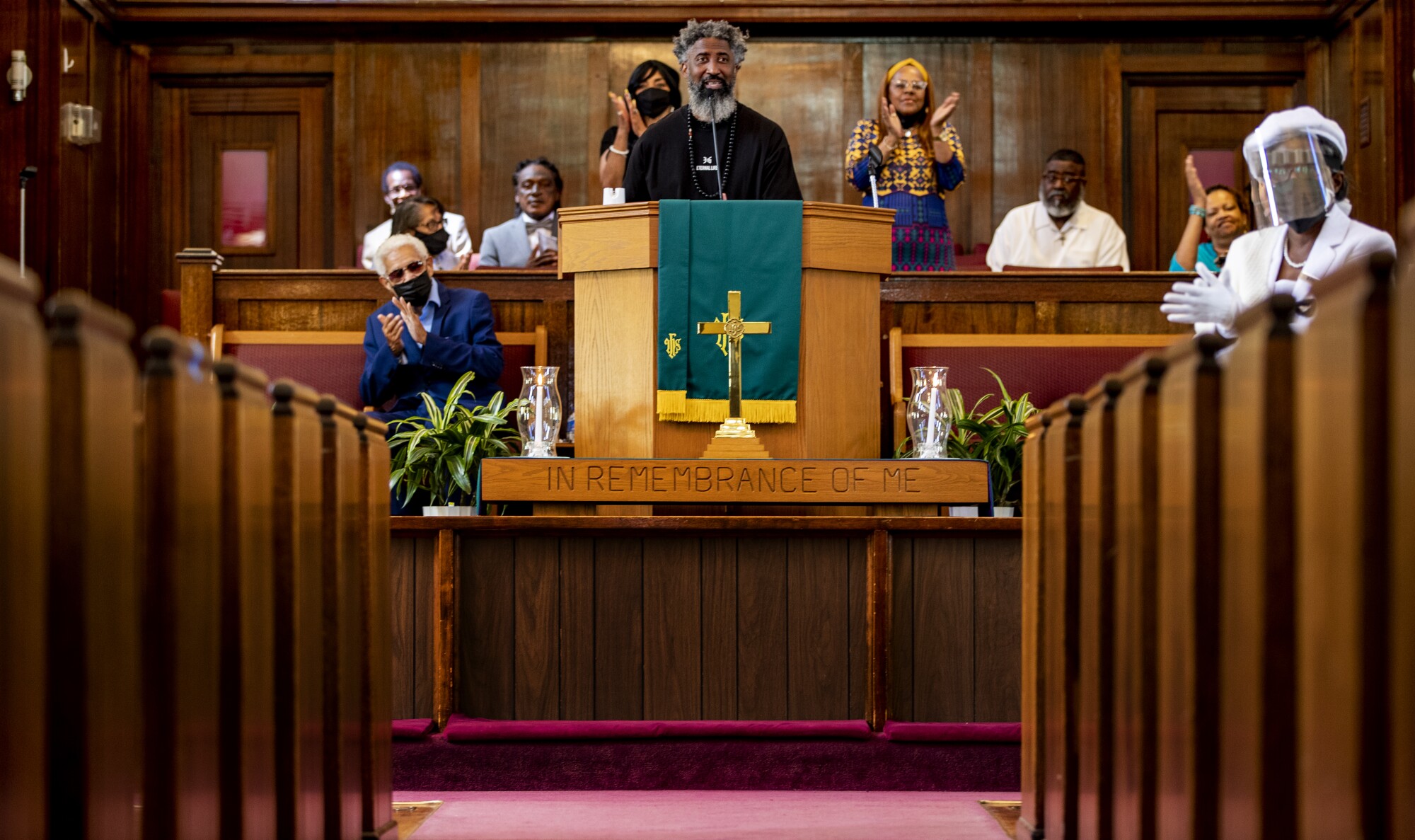 A pastor giving a sermon from a church pulpit as people around him applaud