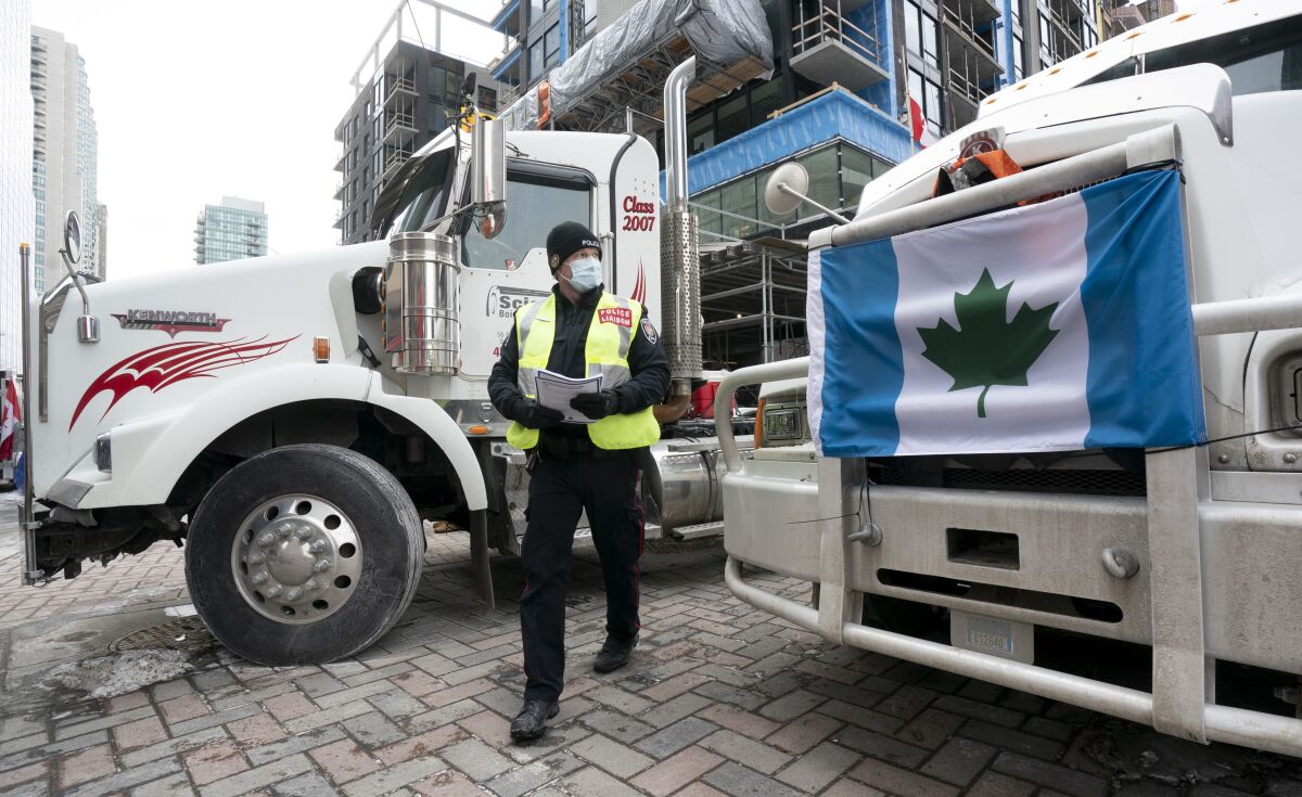 A police officer walks between parked trucks as he distributes a notice to protesters, Wednesday, Feb. 16, 2022 in Ottawa. Ottawa’s police chief was ousted Tuesday amid criticism of his inaction against the trucker protests that have paralyzed Canada's capital for over two weeks, while the number of blockades maintained by demonstrators at the U.S. border dropped to just one. (Adrian Wyld /The Canadian Press via AP)