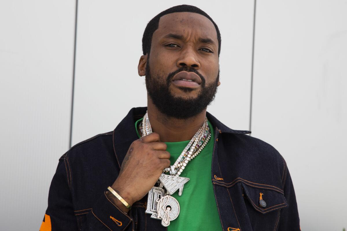 A man in a black jacket and greet T-shirt pulls on several diamond necklaces around his neck.