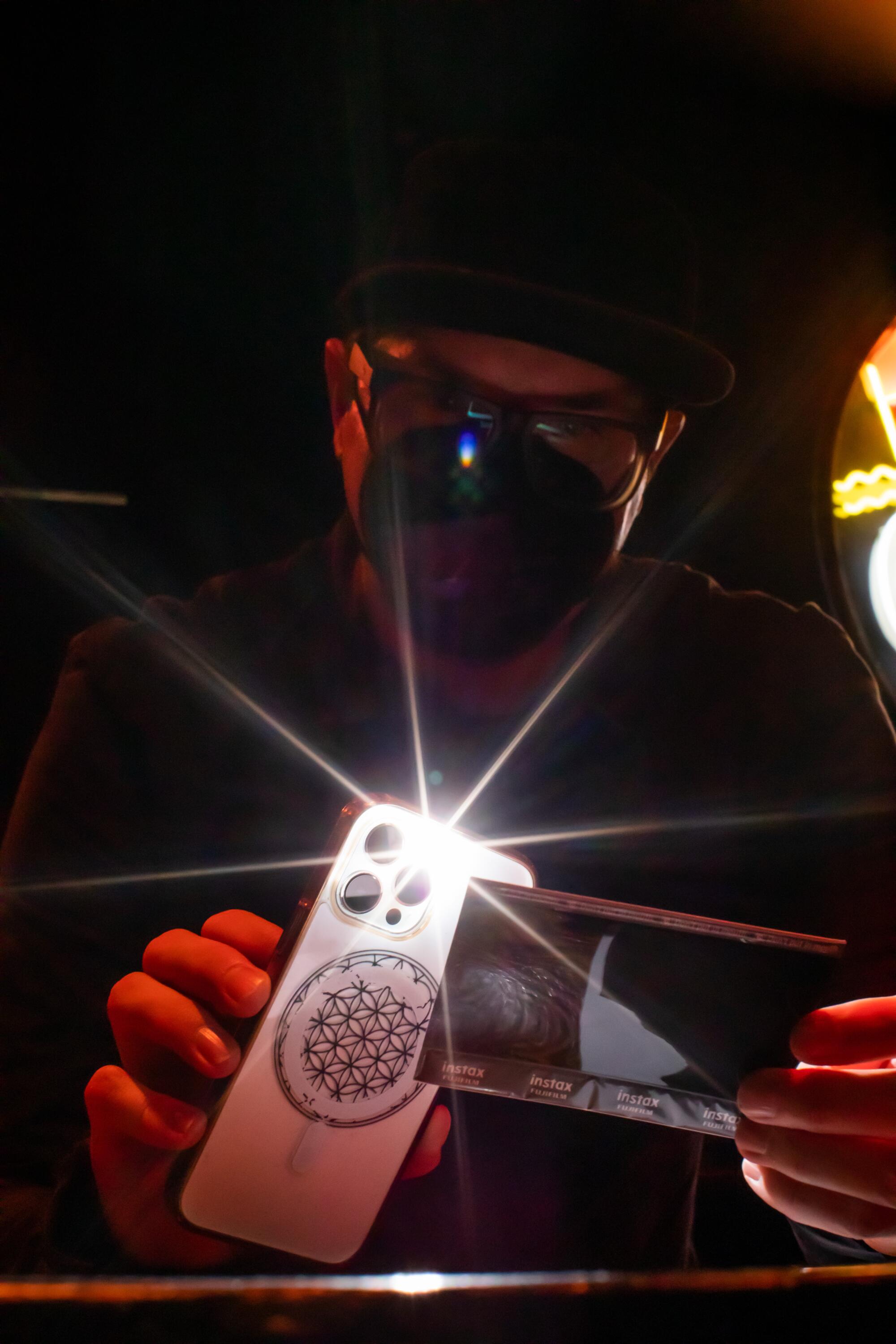 A man in a face mask shines a phone's light onto instant film 