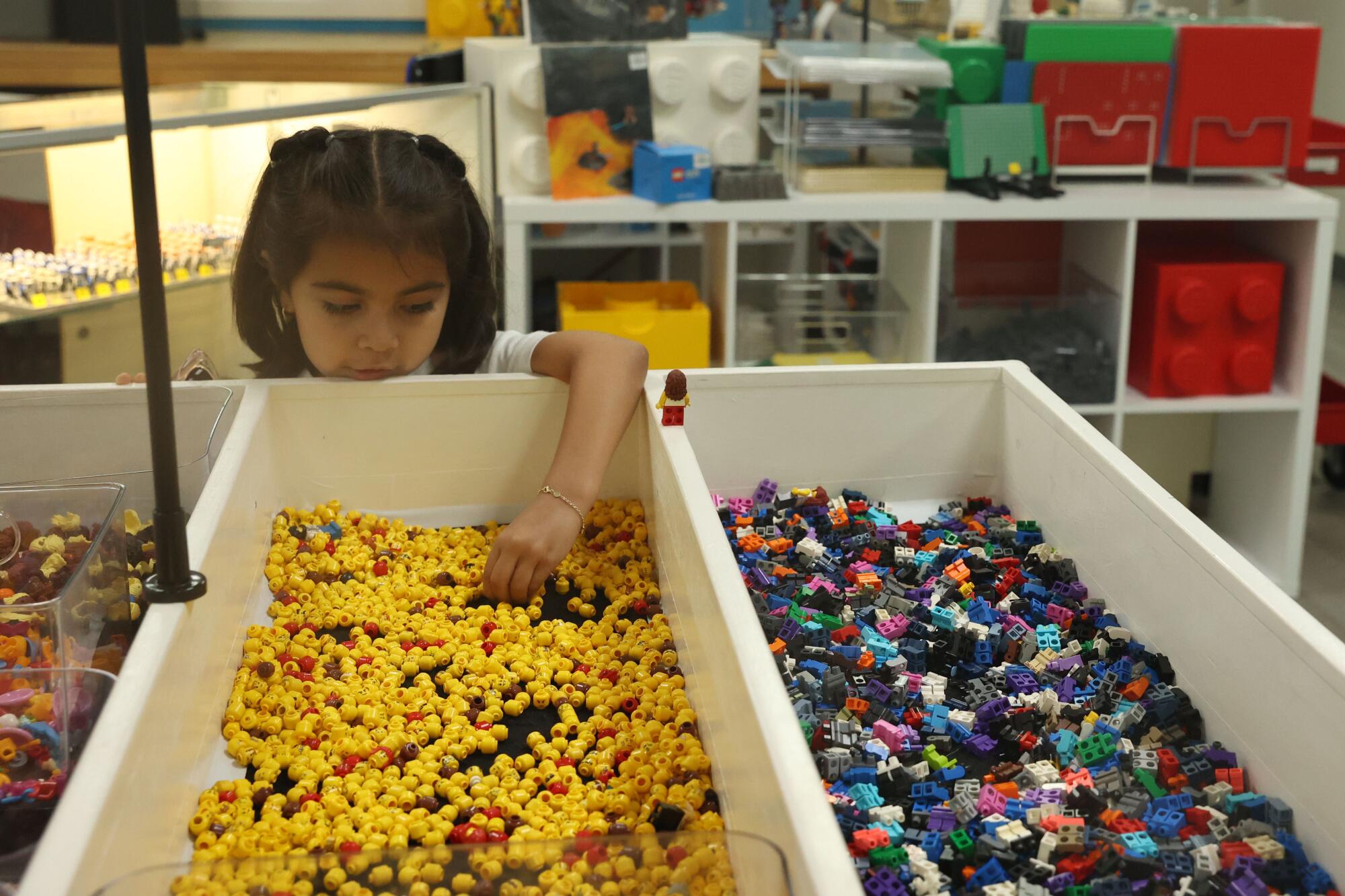 A child reaches into a bin with assorted Lego heads