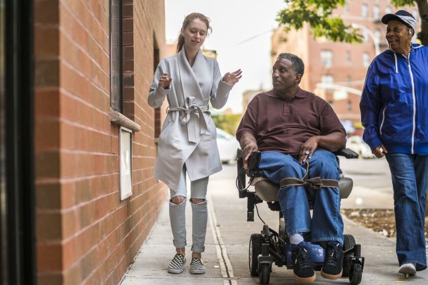 The White teenager girl talking with disabled wheel-chaired African American man and woman when they walking on the street in Bronx, New York, together