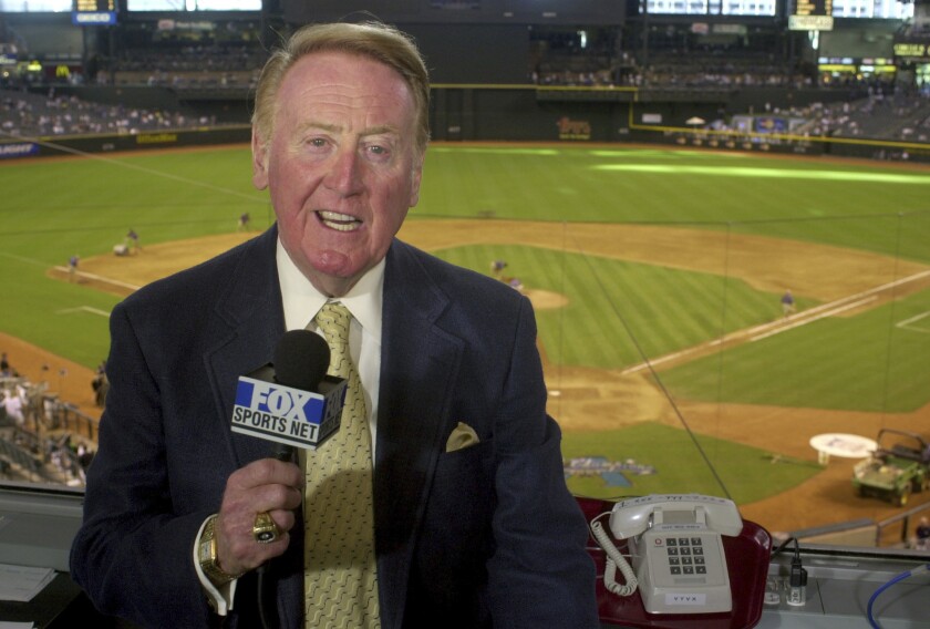 Vin Scully holds a microphone in front of a baseball field.