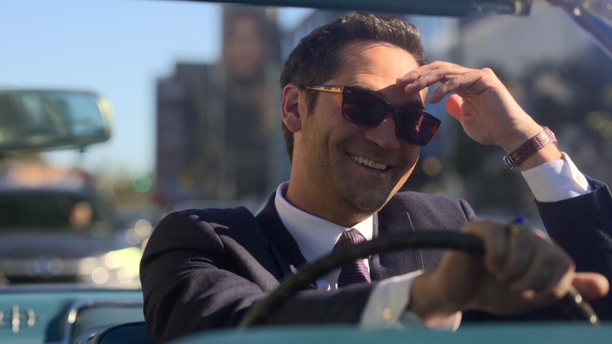 A smiling man in sunglasses driving a convertible.