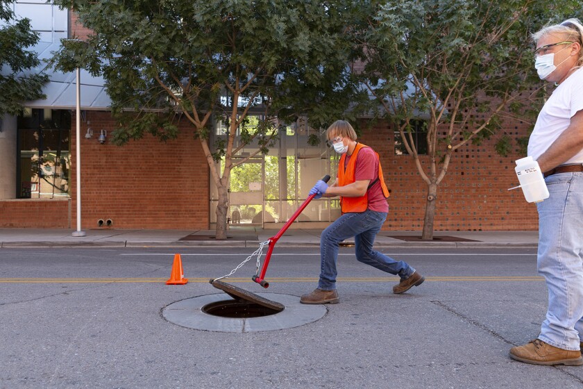 A student opens a manhole cover on a street.