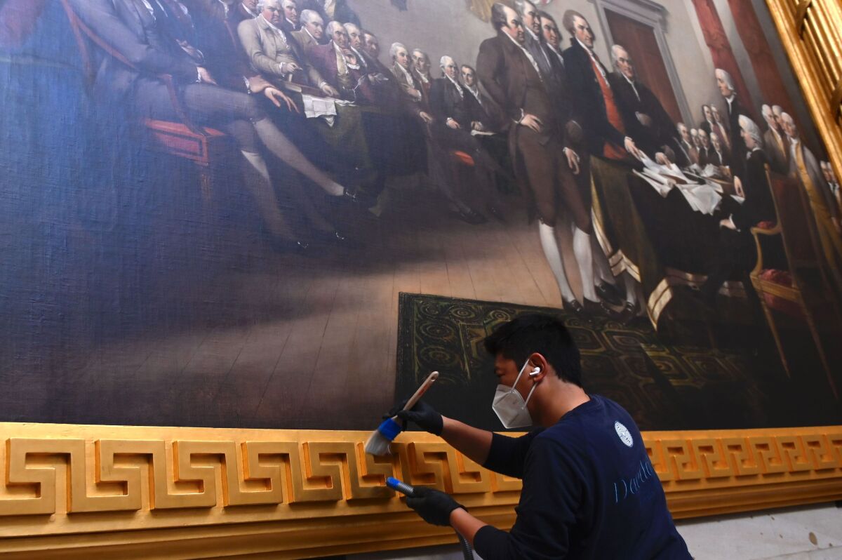 A preservationist uses a brush to clean the gold frame around a painting inside the US Capitol Rotunda.