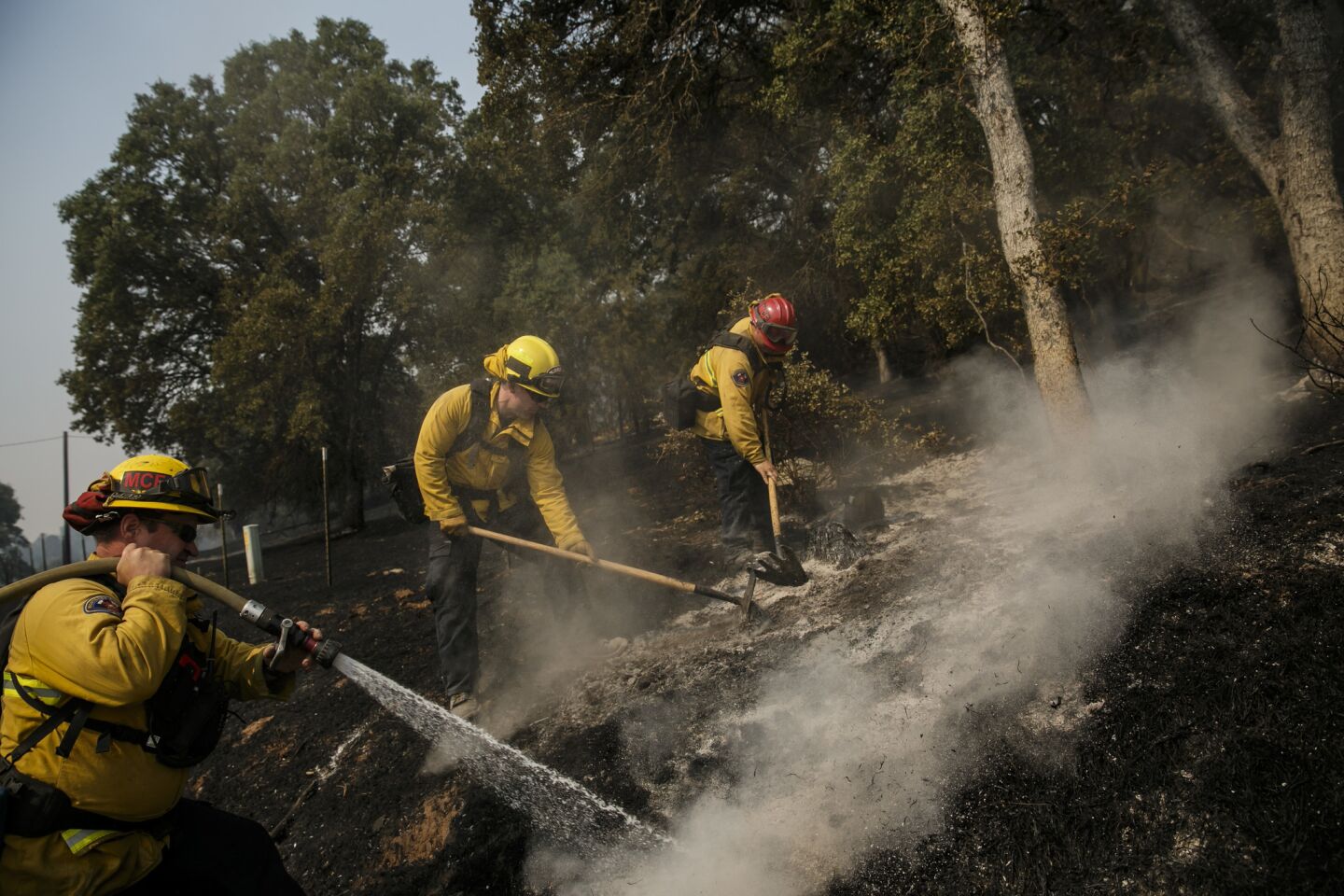 Marc Silva, left, Greg Bodnar and Mike Foster, firefighters from strike team 2800a from Monterey County, mop up hot spots in a residential neighborhood on the outskirts of Mariposa, Calif.