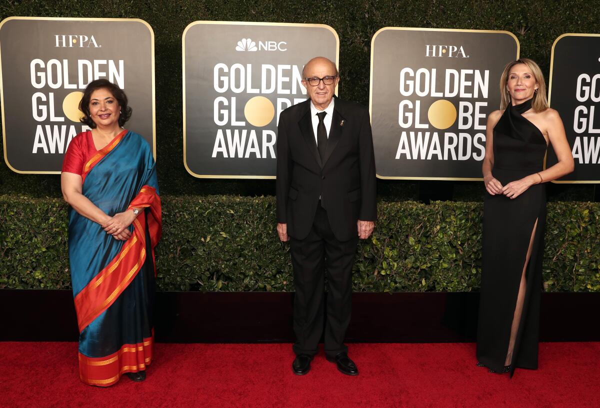 Three people stand on the red carpet at the Golden Globe Awards