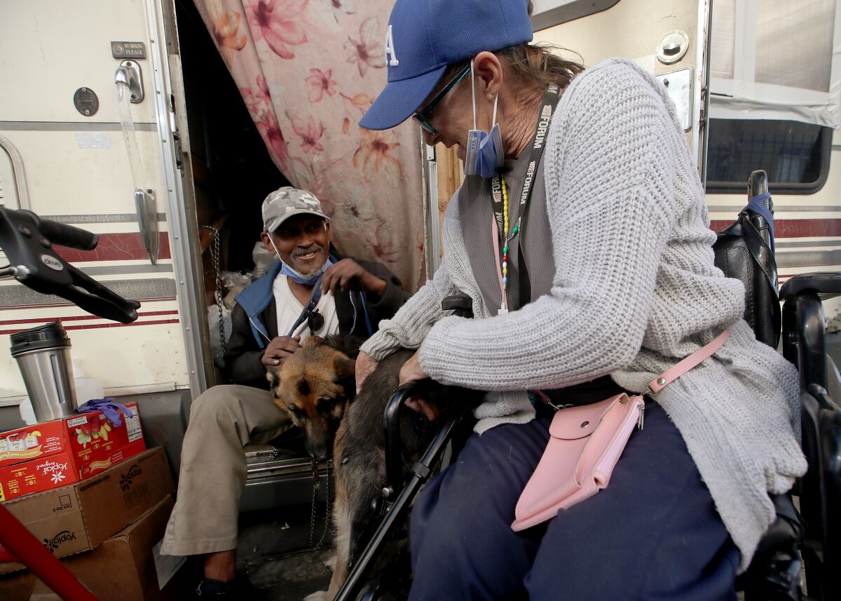 Two people sit outside a motor home with a dog