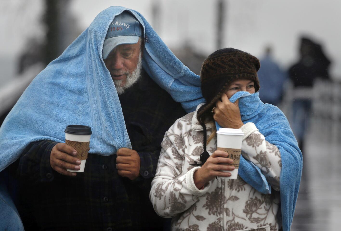 Seal Beach residents Mike and Cookie Castro cover themselves with a giant towel while a light rain falls on their morning walk along the Seal Beach Pier.