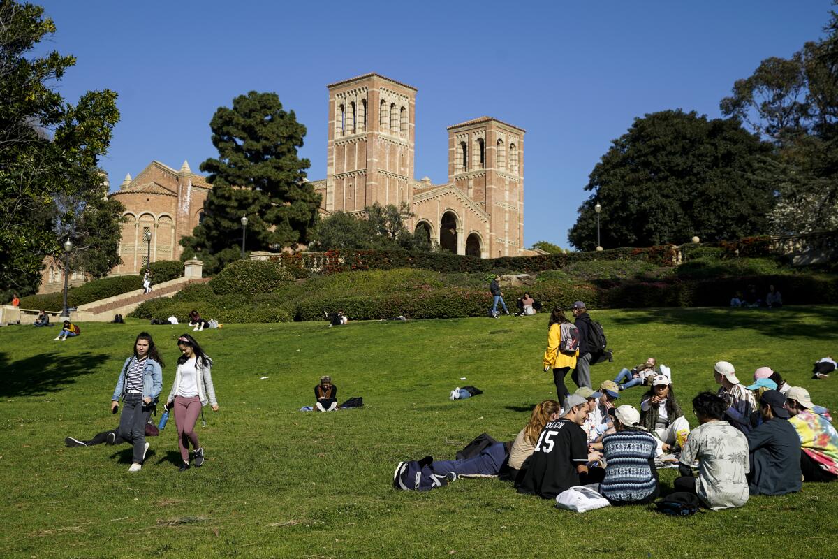 Students walk on and hang out on an expansive green hill on the UCLA campus