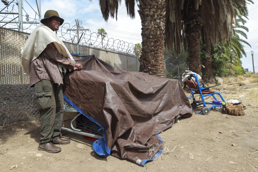 Charles Patterson, 69, who says he's been homeless for five years, ties down a tarp at his encampment that is nearby the proposed storage area site for homeless people's belongings, located next to Chollas Parkway, on Wednesday, September 25, 2019 in San Diego, California. Patterson said he would use the storage site if he could be reassured that his belongings would be safe there.
