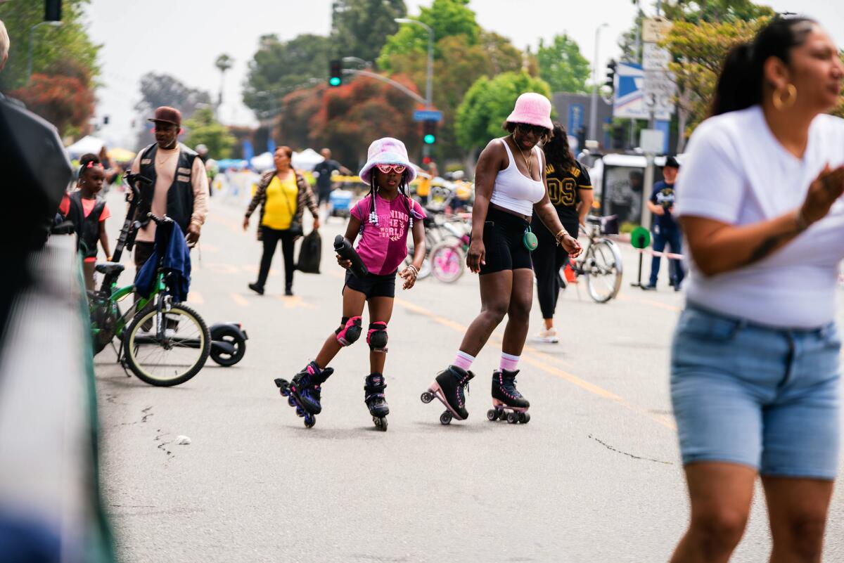 A girl in-line skating and a woman roller skating in the street.