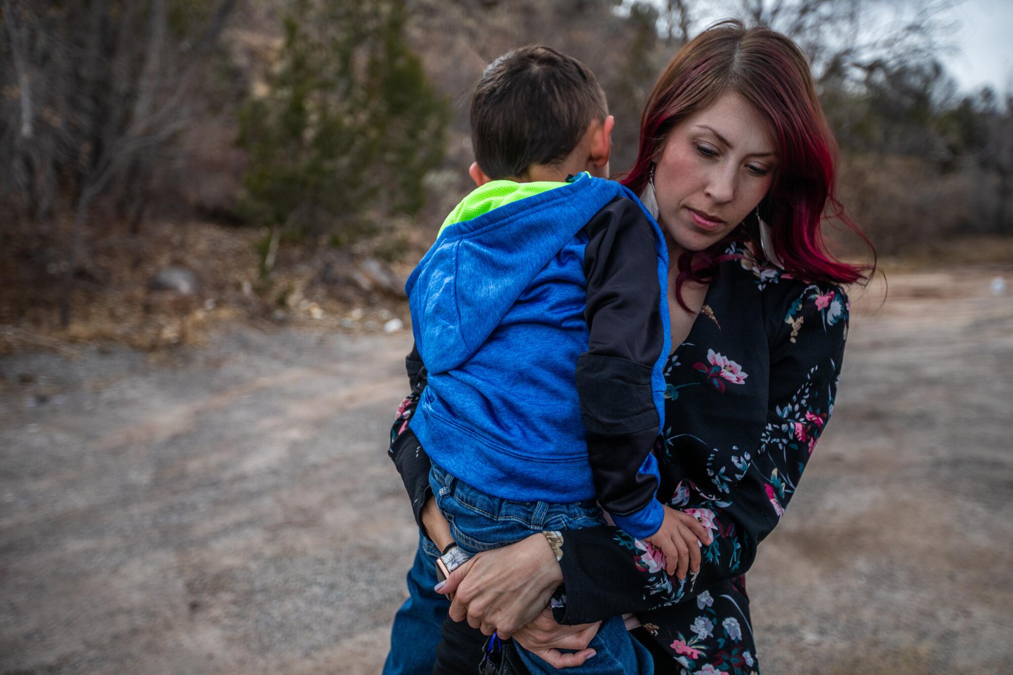 A woman holds a child while standing on a dirt path