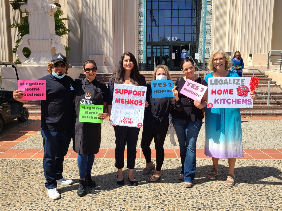 Six women hold signs supporting home kitchens, while outside the San Diego County administration building