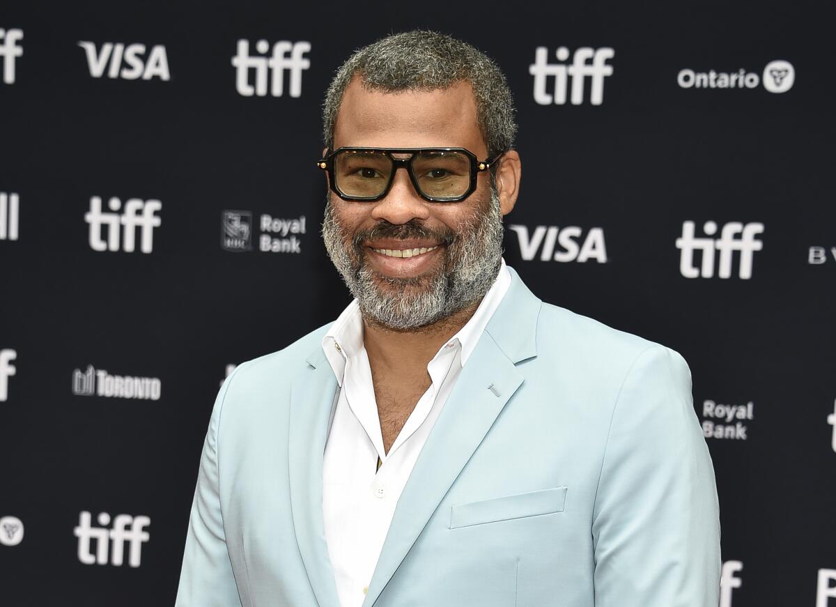 A gray-bearded man wearing dark sunglasses and a light blue suit