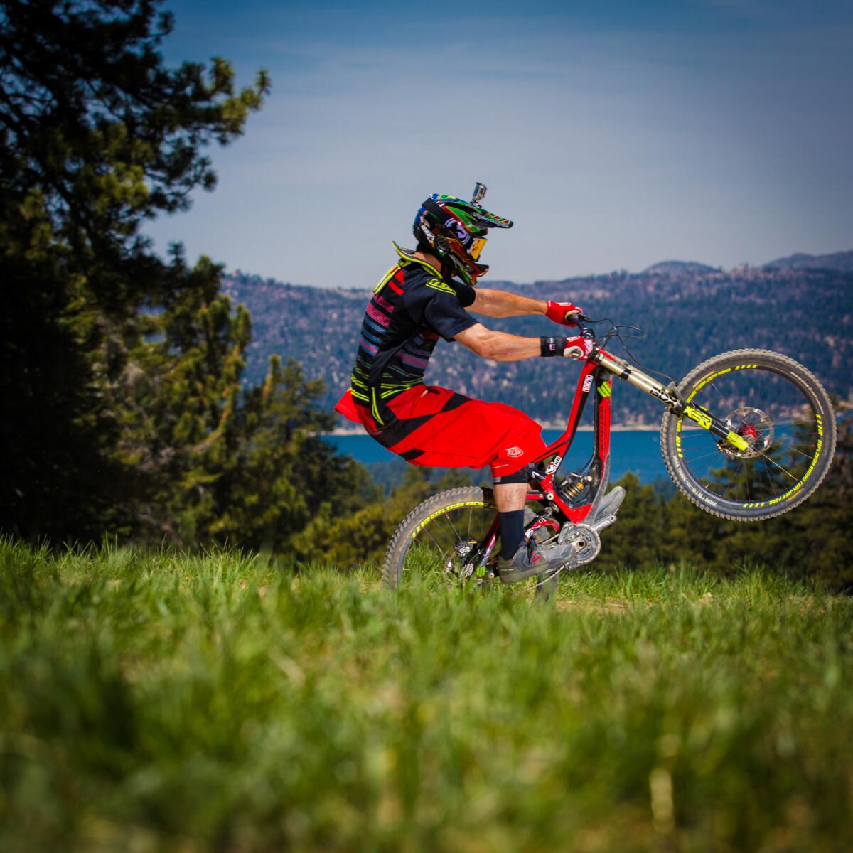 Man on a red bike wearing a helmet and popping a wheelie. 