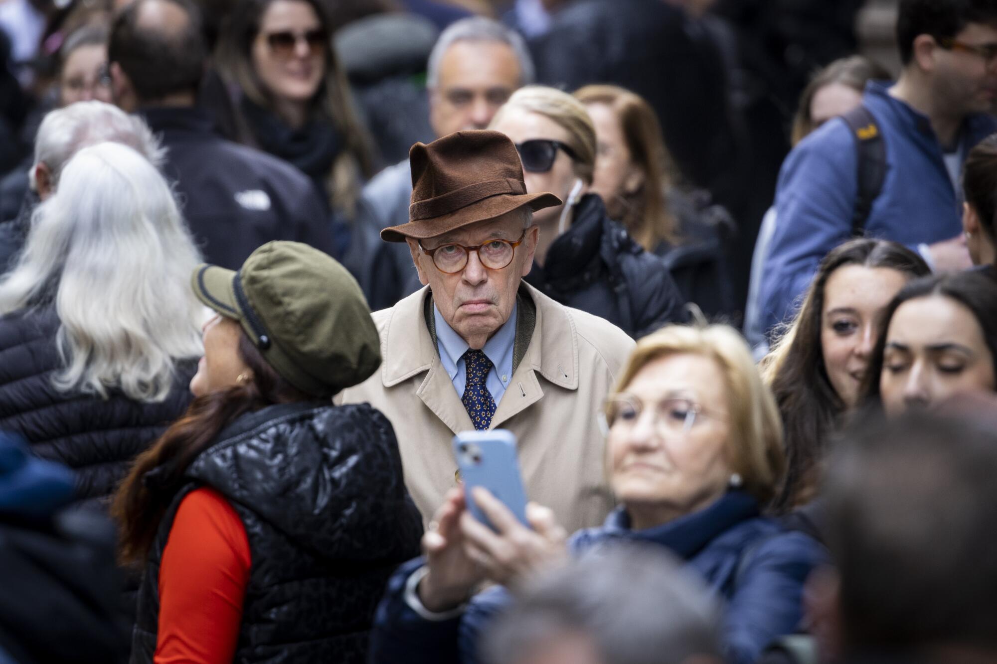 A man in a hat looks disgruntled as people crowd a sidewalk.