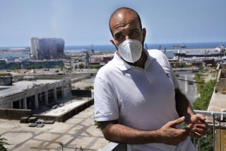 Johnny Assaf who was injured during the massive 2020 Beirut's massive explosion, and who runs a small real estate agency, stands on his office balcony, wearing a face mask after the Lebanese Environment and Health Ministries warned residents living in neighborhoods near the Beirut Port to wear masks and to stay indoors, as one of its mammoth grain silos, seen in the background, may partially collapse, in Beirut, Lebanon, Thursday, July 28, 2022. Emmanuel Durand, a French civil engineer who volunteered for the Lebanese government-commissioned team of experts says it is inevitable that the north block going to collapse. (AP Photo/Hussein Malla)