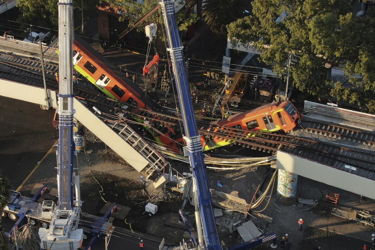 An aerial view of subway cars dangle at an angle from a collapsed elevated section of the metro