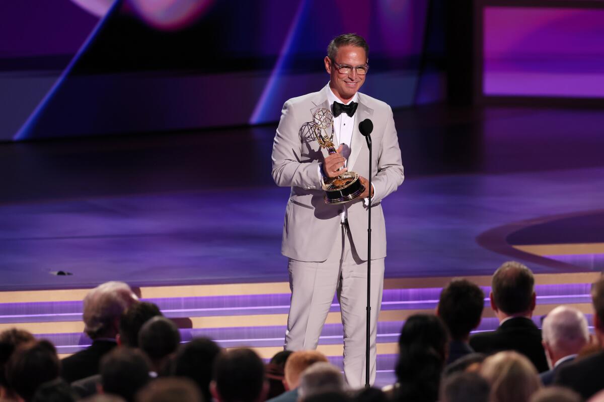 A man in a light colored suit and black bowtie speaking into a microphone.