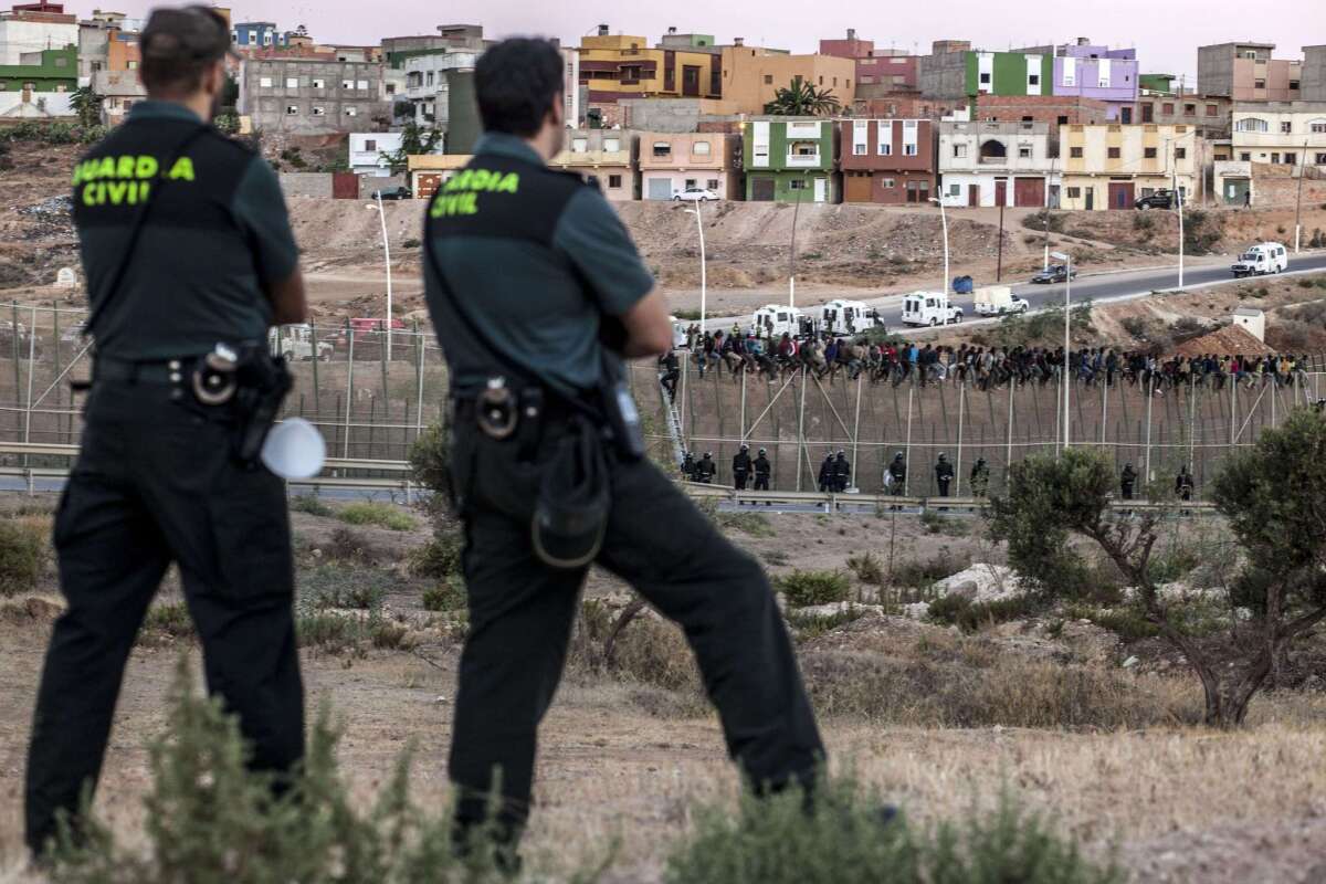 Spanish Guardia Civil watch as would-be immigrants from Africa sit atop a fence after scrambling over two other border barriers on Spain's tiny north African territory of Melilla.