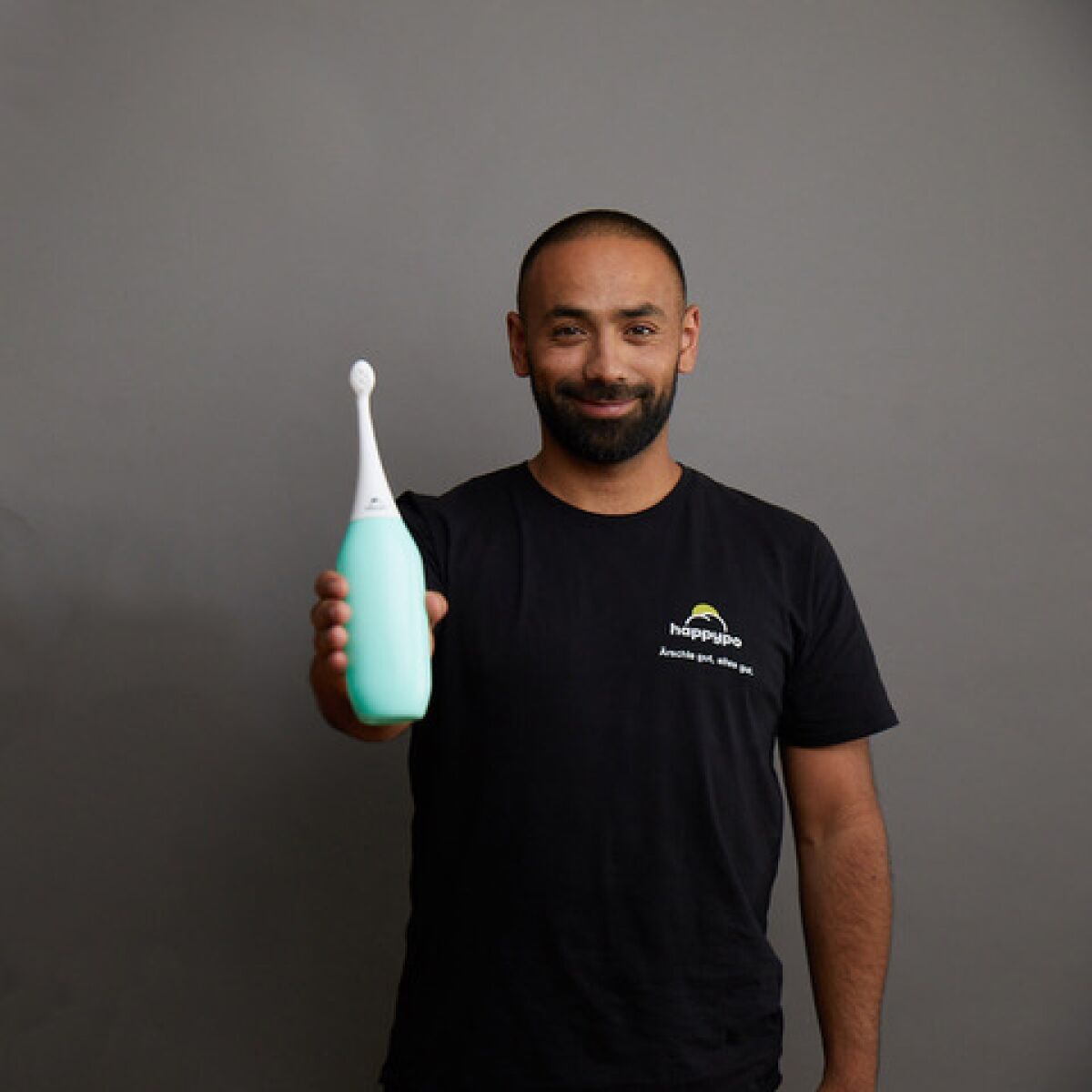 A man in a T-shirt that says "Happy Po" smiles as he holds out his product, a large squeeze bottle.