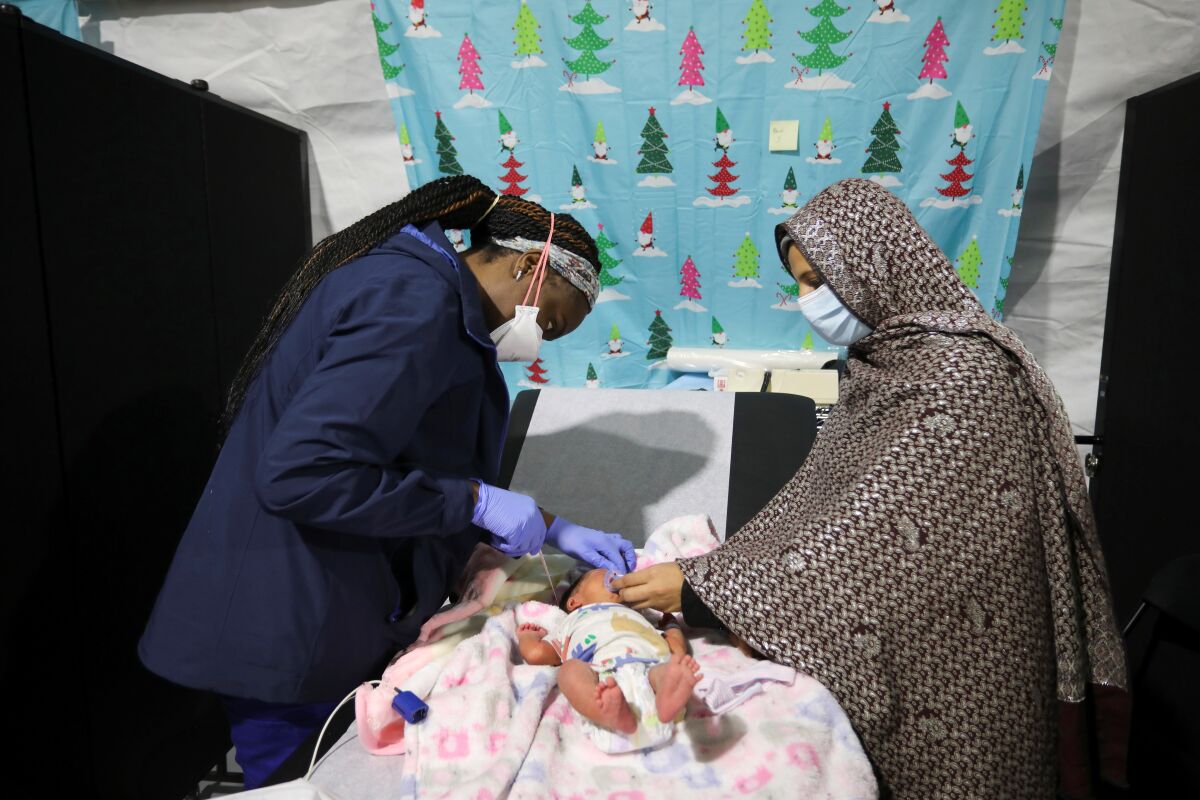 A nurse, left, attends to an infant as the child's mother, right, looks on 
