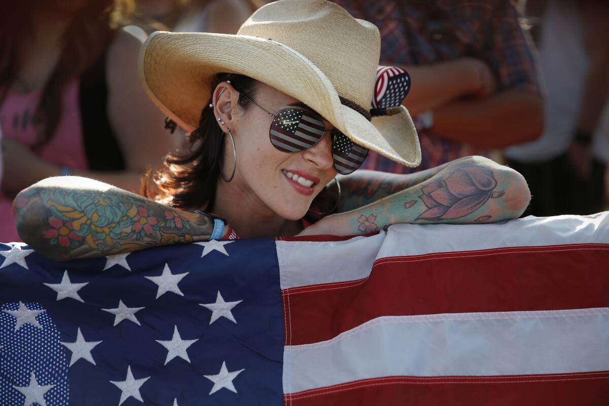 Lindsay German of Ventura, sporting American flag sunglasses while toting a large U.S. flag, listens to music at the Mane Stage during the first day of the 10th Stagecoach Country Music Festival.