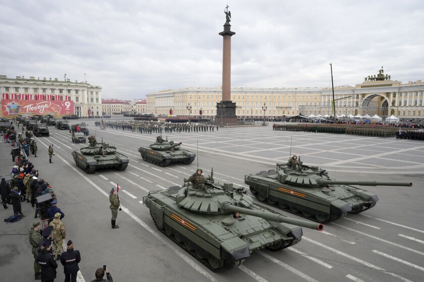 Two rows of tanks and military vehicles drive along a huge square.